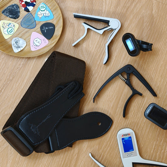 Collection of guitar accessories including picks, capos, and a tuner on a wooden surface.
