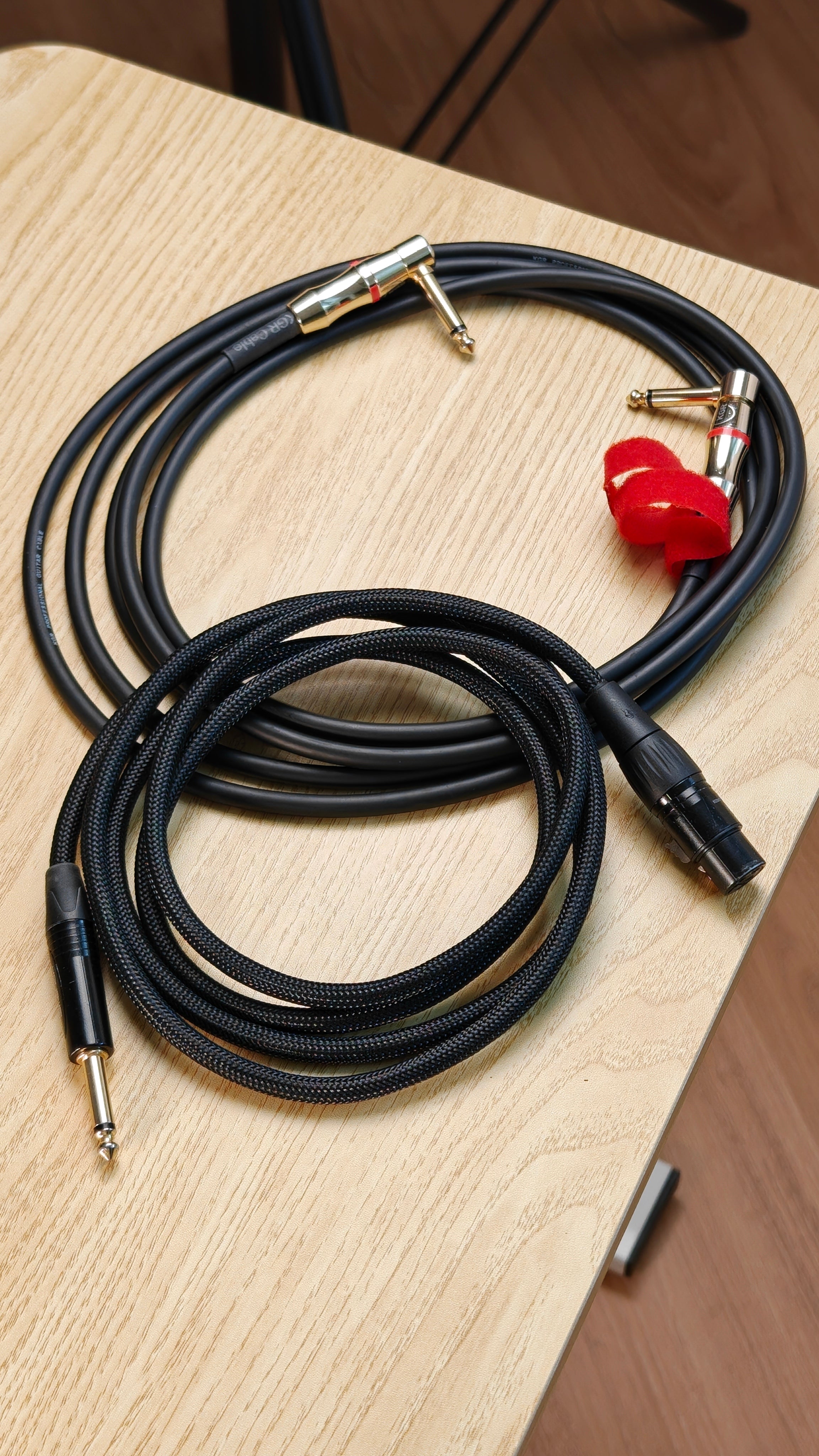 Black audio cables with gold connector on a wooden surface. Guitar Jack and a XLR Cable