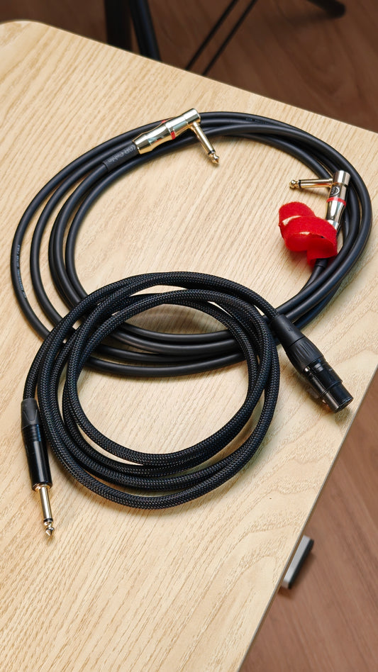 Black audio cables with gold connector on a wooden surface. Guitar Jack and a XLR Cable