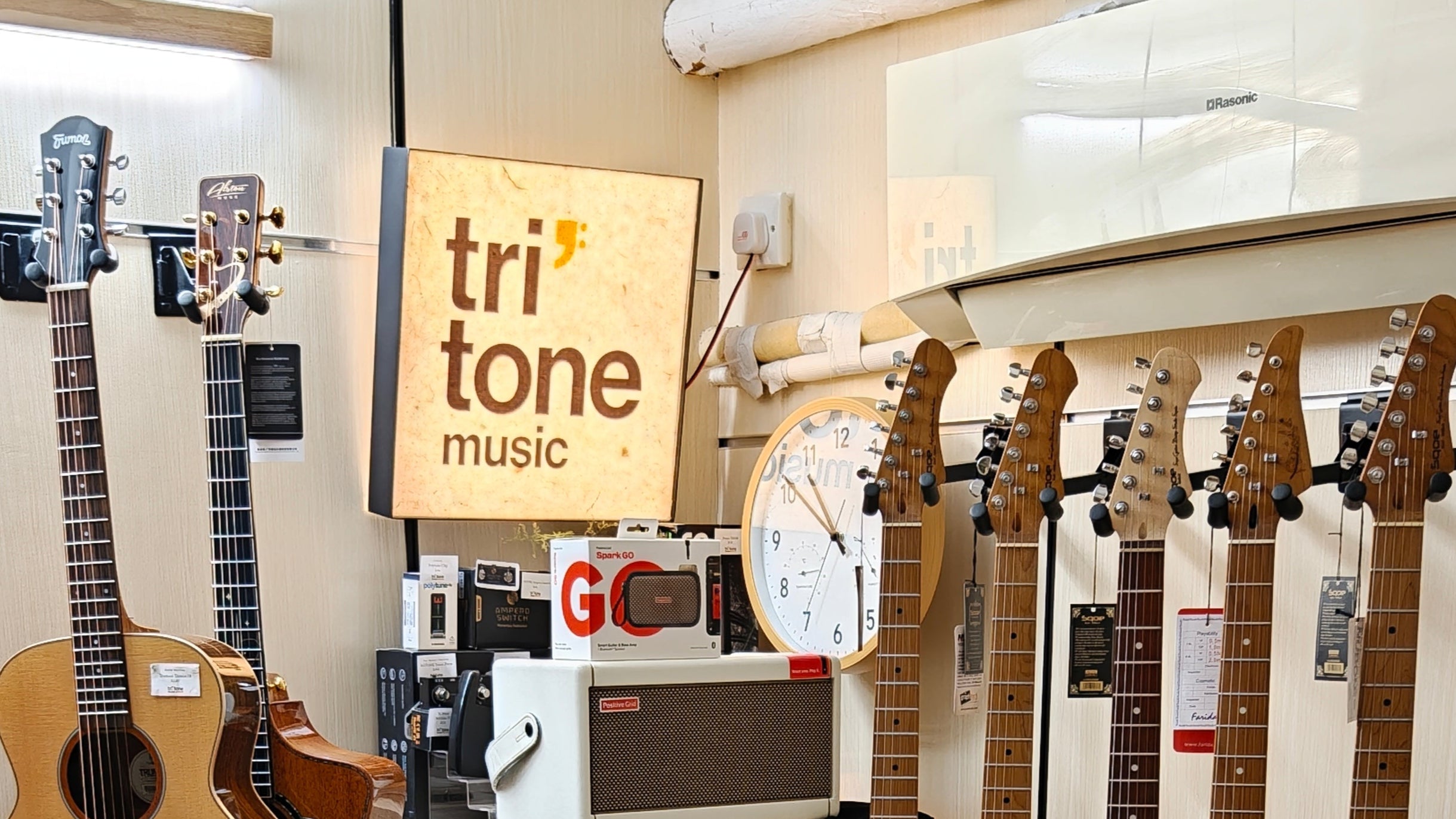 Music store interior with guitars on display, a 'Tritone Music' sign