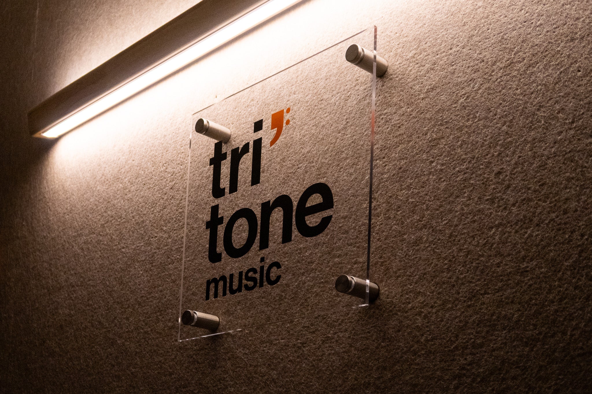 Clear sign with 'tritone music' on a textured wall.