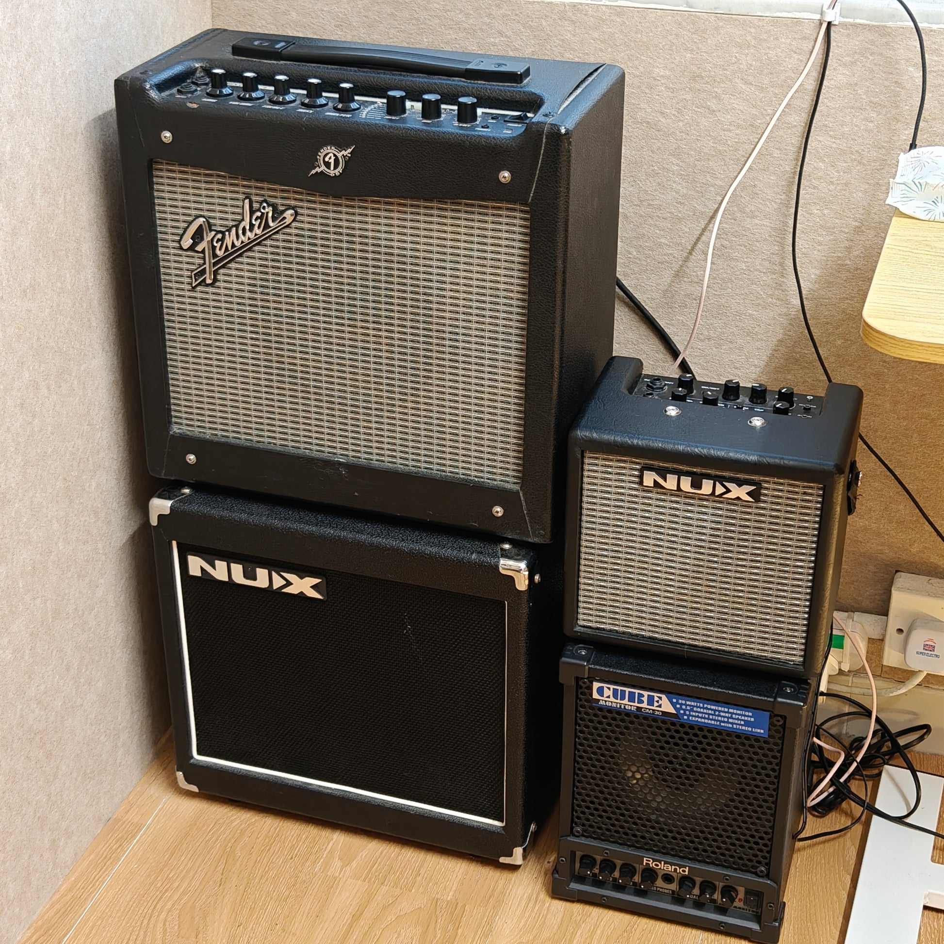 Stack of Fender and Nux guitar amplifiers on a wooden floor against a wall for rent at Tritone Music